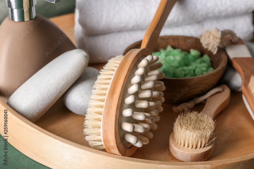 Massage brushes with cosmetics on wooden tray, closeup