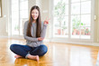 © Krakenimages.com - Beautiful Asian woman sitting barefoot on the floor at home smiling with happy face winking at the camera doing victory sign. Number two.