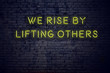 Positive inspiring quote on neon sign against brick wall we rise by lifting others