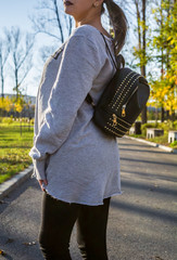 Wall Mural - Woman in gray sweatshirt and black leggings wearing a leather backpack as accessory. Autumn and casual style. Blurred background.