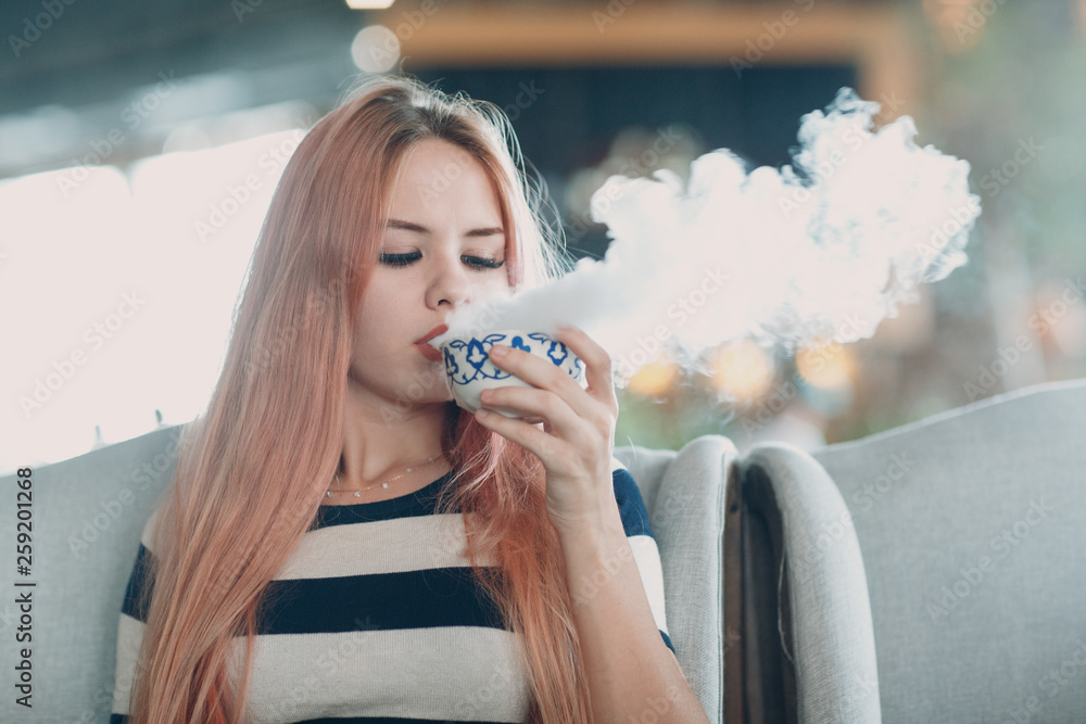 Young pretty girl drinks hot smoking tea in cafe. Stock Photo