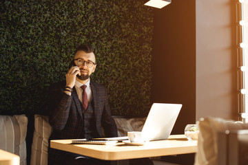 Young handsome man sitting in office with cup of coffee and working on project connected with modern cyber technologies. Businessman with notebook trying to keep deadline in digital marketing sphere.