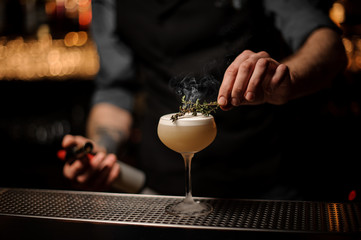 Bartender adds rosemary in alcohol light brown cocktail