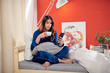© chika_milan - Gorgeous brunette in blue pajamas sitting on bed in bedroom with legs crossed, drinking morning coffee and using smart phone.