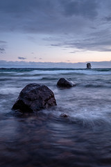 Wall Mural - two large stones stand out from the surface of the beach, a small island in the background