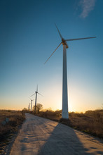 Line Of Wind Turbines Along The Dirt Road At The Sunset