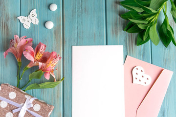 Mock up blank paper on blue wooden background with natural flowers of pink color. Blank, frame for text. Greeting card design with flowers. Aalstroemeria on wooden background. Flat lay, top view.