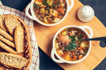 Two plates with lentil soup and chicken on a wooden board on black table, top view