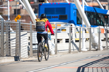 Wall Mural - Woman with backpack and jacket rides bike on the bridge next to the bus preferring healthy lifestyle