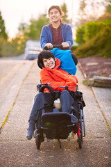 Sister pushing disabled little brother in wheelchair around neighborhood