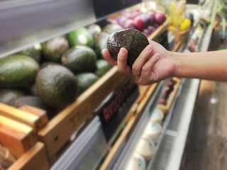 Woman's hand holding avocado for choose from the shelf in the supermarket.