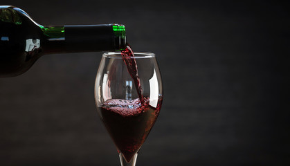 Wall Mural - Pouring red wine into the glass against wooden background