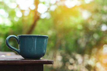 Wall Mural - green mug of hot drink put on wooden table in nature of morning day