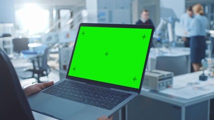 Aufkleber - Engineer Holds Green Mock-up Screen Laptop Computer. In the Background Team of Industrial Engineers Working with Functional Robot Arm in Modern Bright Research Facility