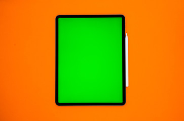 Wall Mural - new tablet on a Orange background with a keyboard and pen, and green screen top view