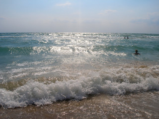 Foamy wave on a sandy beach with bathing people. Black Sea. Sunny day. Summer