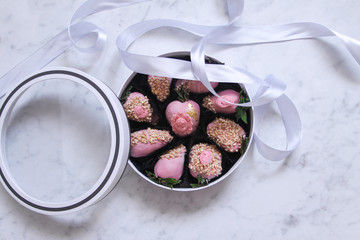 Wall Mural - Strawberries covered with pink chocolate icing with nuts in a round box with a transparent lid with a gray ribbon and a bow on gray marble