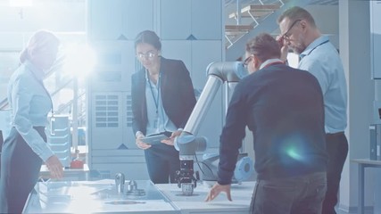 Leinwandbilder - Diverse Team of Industrial Robotics Engineers Gathered Around Table With Robot Arm, They Manipulate and Program it to Pick Up and Move Metal Component.
