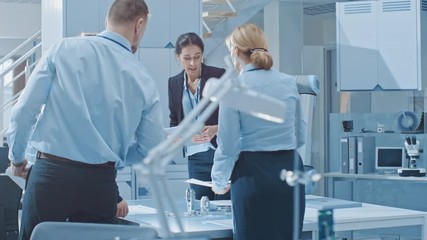 Aufkleber - Diverse Team of Industrial Robotics Engineers Gathered Around Table With Robot Arm, They Use Tablet Computer to Manipulate and Program it to Pick Up and Move Metal Component. Bright Facility
