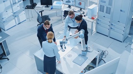Leinwandbilder - Team of Industrial Robotics Engineers Gathered Around Table With Robot Arm, They Use Tablet Computer to Manipulate and Program it to Pick Up and Move Metal Component