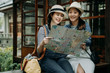 © PR Image Factory - two female asian tourist with paper map sitting in bench by japanese style garden wooden house. Beautiful smiling girl friends traveler holding guide in hands discussing while travel kyoto japan