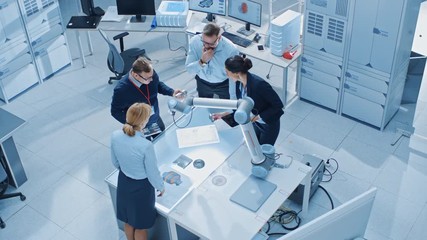 Aufkleber - Team of Industrial Robotics Engineers Gathered Around Table With Robot Arm, They Use Tablet Computer to Manipulate and Program it to Pick Up and Move Metal Component. Top Down Above Shot
