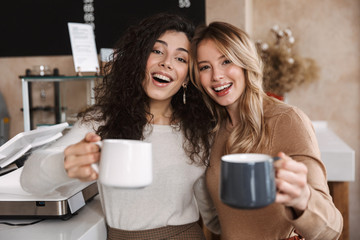 Canvas Print - Happy girls friends sitting in cafe talking with each other drinking tea or coffee.