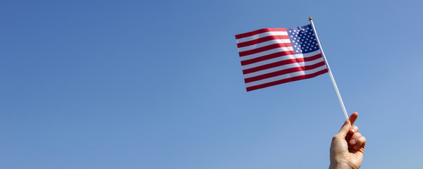 Boy hand holding American flag against  blue sky