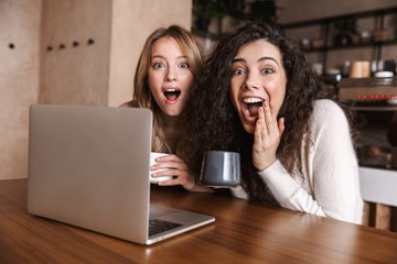 Wall Mural - Emotional shocked girls friends sitting in cafe using laptop computer.