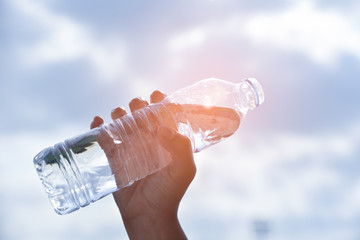  Woman hand holding a drinking water bottle on blue sky background in the morning with sunlight. Cool drinking water. World Water Day concept.