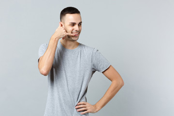 Pleasant young man in casual clothes looking aside doing phone gesture like says call me back isolated on grey wall background in studio. People sincere emotions lifestyle concept. Mock up copy space.