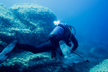 person diving at blue sea near the bottom rocks