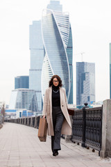 Beautiful business woman in a long light coat comes with a case in his hand on the waterfront