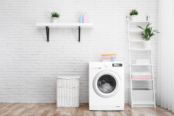 Modern washing machine near brick wall in laundry room interior, space for text