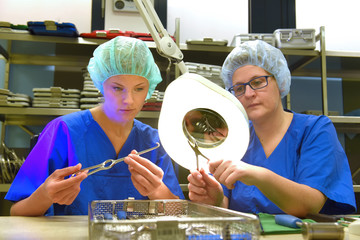 Two women work in a hospital as medical hygiene  technicians. They are dressed in special medical  hygiene clothing. They are seen carrying out hygiene  disinfecting and sterilization tasks.