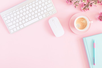 Office pink table, notepad, keyboard, flowers, coffee, notebook, stationery on pink background. Business minimal concept for women. Flat lay, top view, copy space 