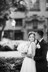 Wall Mural - Elegant bride in a white dress and veil. Handsome groom in a blue suit. Couple in a summer park