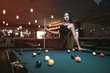 © RomanR - Beautiful woman in black dress posing with billiard cue