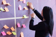 © as-artmedia - Smiling young female employee in stylish spectacles using stickers for creation strategy of working project during brainstorming session, skilled team member making notes presenting idea of startup.