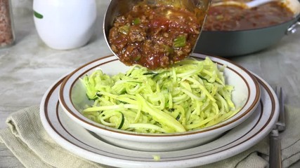 Canvas Print - Spooning spaghetti sauce onto a bowl of zucchini noodles