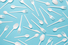 Plastic Disposable Forks And Spoons On A Blue Background. Abstract Background Of Plastic Utensils.