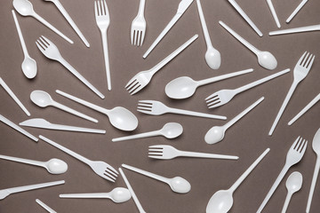 Plastic disposable forks and spoons on a brown background. Abstract background of plastic utensils.