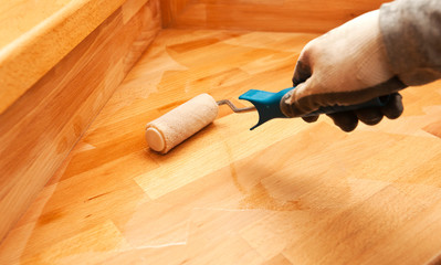 The painter  paints a varnish wooden board by roller