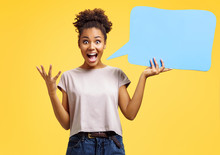 Overjoyed Girl Holds Blue Speech Bubble Board. Photo Of African American Girl Wears Casual Outfit On Yellow Background. Emotions And Pleasant Feelings Concept.