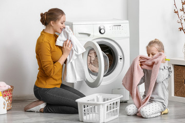 Young woman and her little daughter doing laundry at home