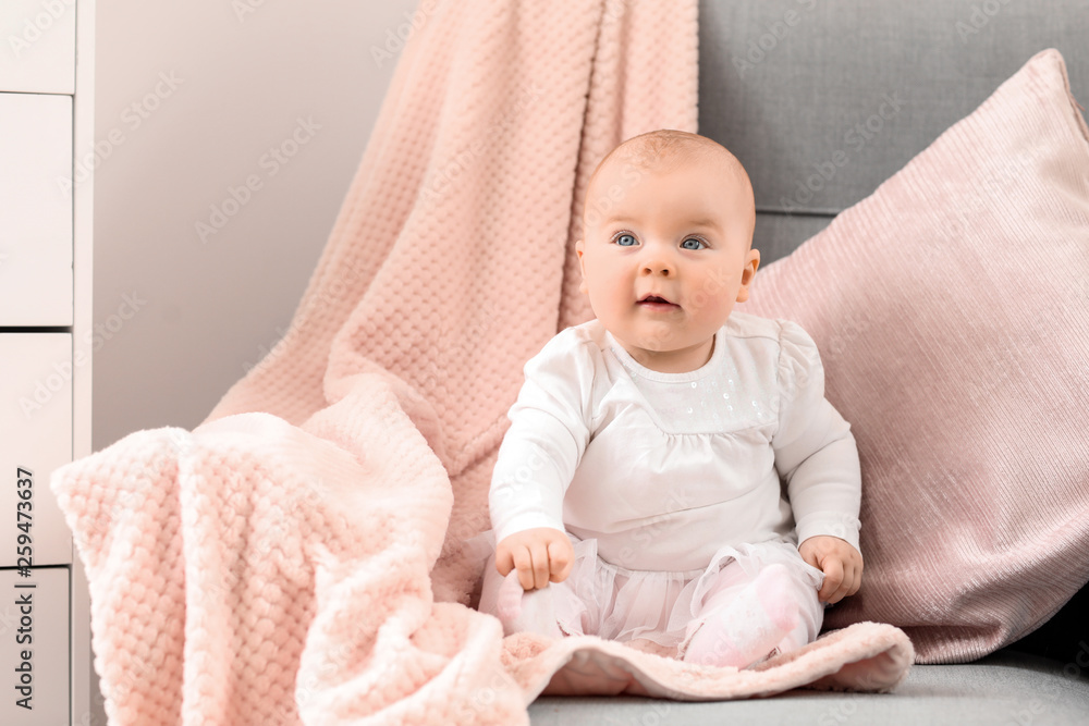 Adorable baby girl sitting on sofa at home