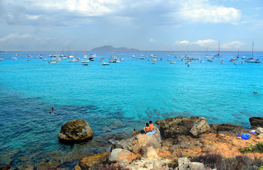 people inside paradise clear torquoise blue water with boats and cloudy blue sky in background in Favignana island, Cala Rossa Beach, Sicily South Italy.