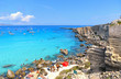 people inside paradise clear torquoise blue water with boats and cloudy blue sky in background in Favignana island, Cala Rossa Beach, Sicily South Italy.