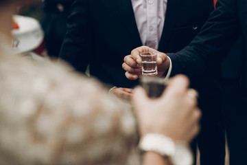 Wall Mural - people holding glasses of vodka and toasting at wedding reception, celebration outdoors, catering in restaurant. christmas and new year