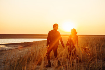 Enjoying time together.  Stylish and loving couple enjoying each other by the sea. The couple is young and in love. The concept of youth, love and lifestyle. Beautiful sunset on a summer day.